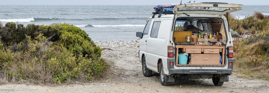 Weißer Van mit geöffneter Heckklappe am Strand